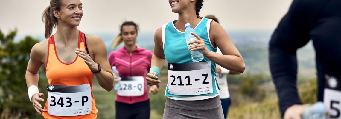 Happy female runners talking while running marathon in nature.